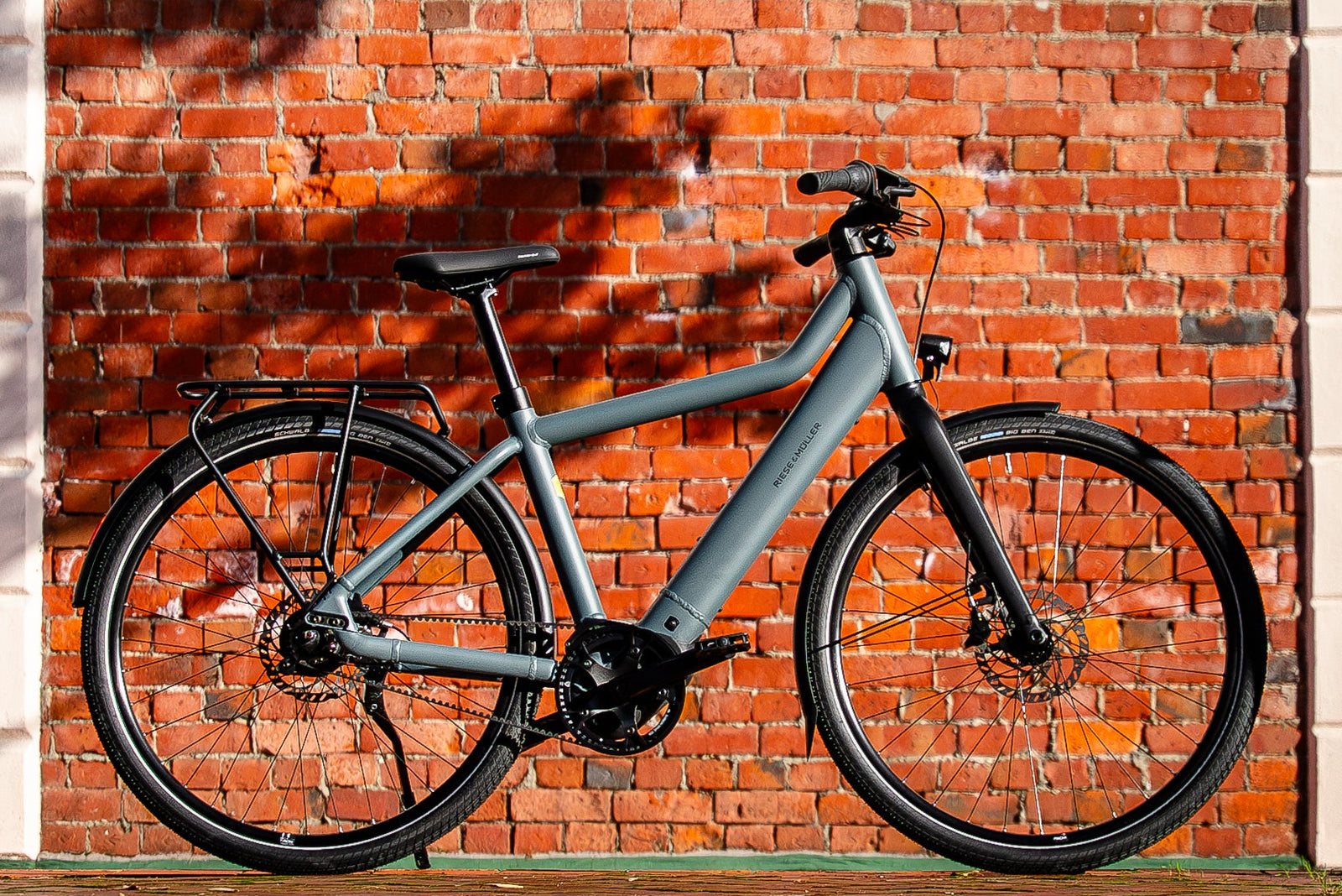 Gray electric bicycle leaning against a red brick wall.