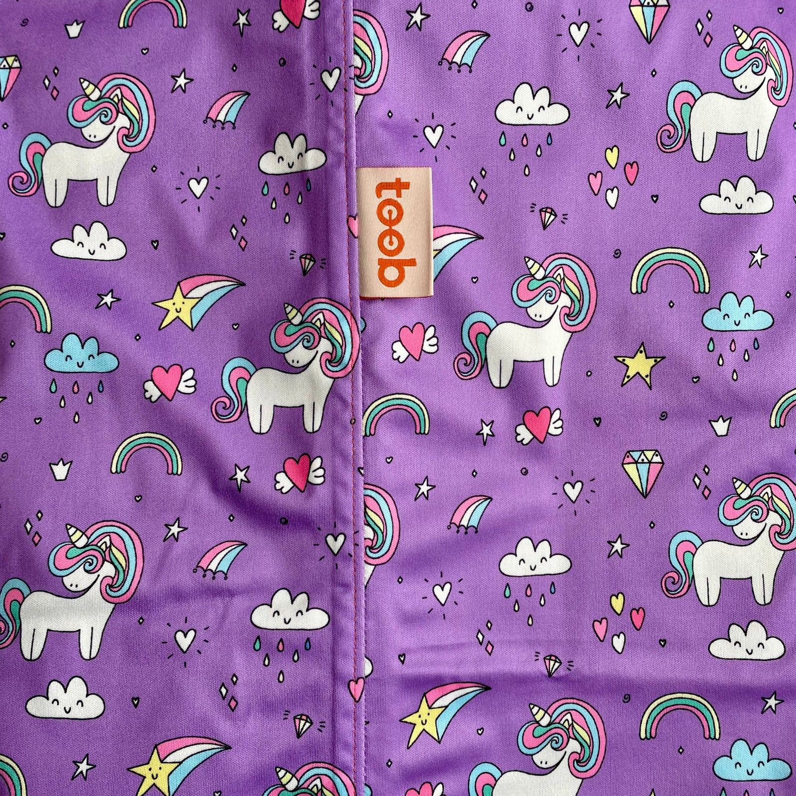 Purple fabric with unicorn, rainbow, and heart patterns, featuring the brand 'Teo'.