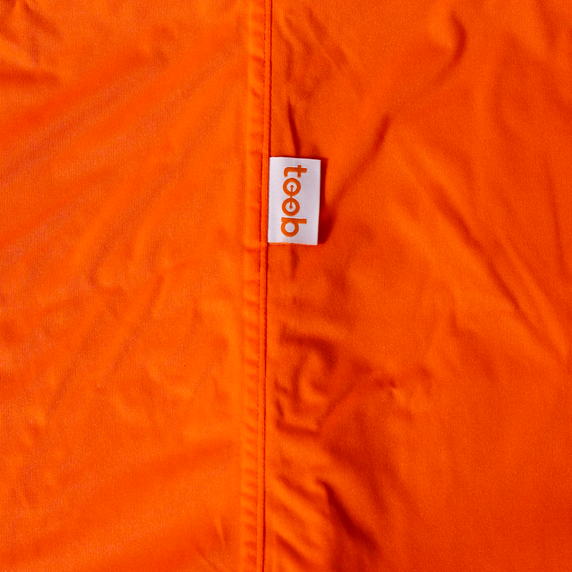 Close-up of an orange jacket with a 'toeb' logo on a white background