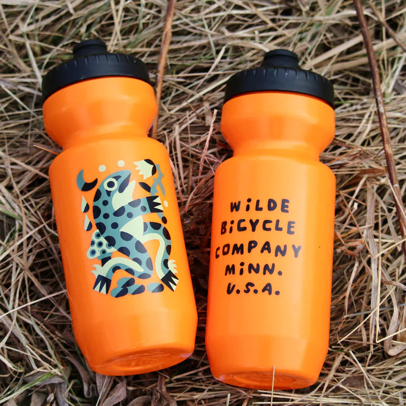 Two orange water bottles with black lids on dry grass