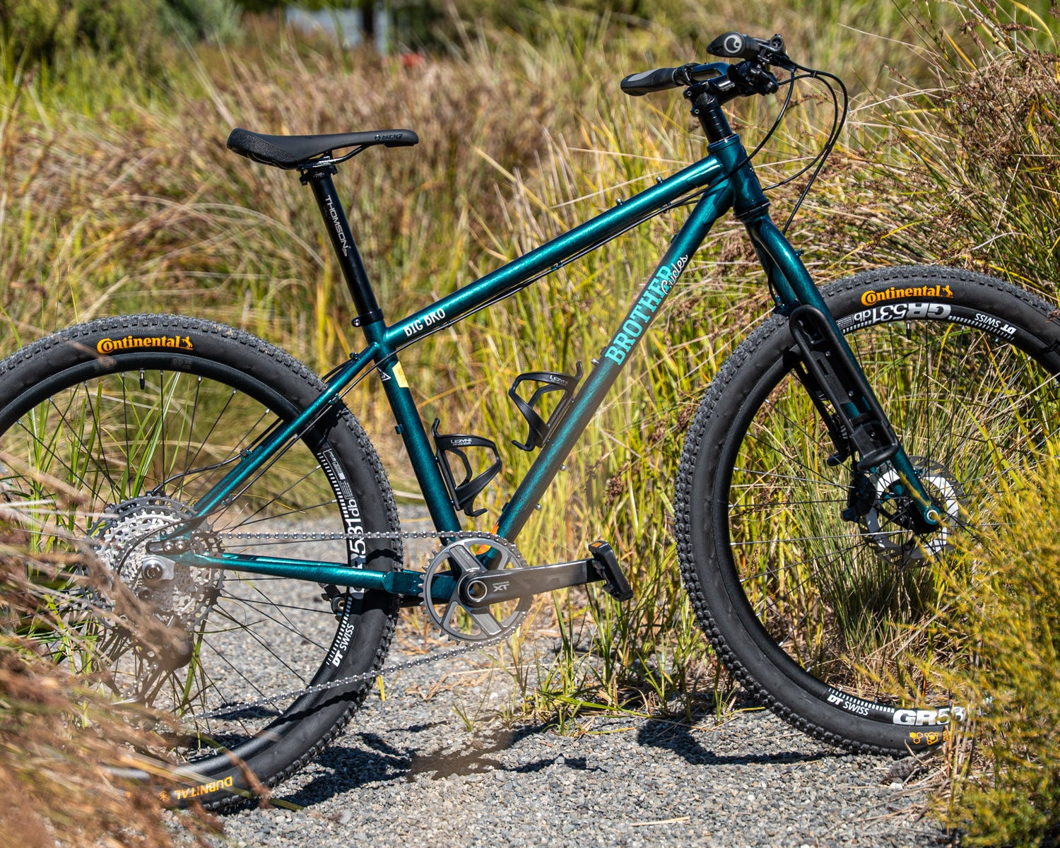 Teal bicycle with black components on a gravel path surrounded by grass